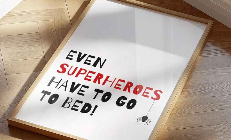 May include: A framed print with the text "Even superheroes have to go to bed!" in black and red lettering. A black spider with a red body hangs from a string above the text.