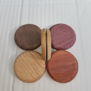 May include: Five wooden discs in various shades of brown, purple, and red. The discs are arranged in a circle with one disc standing upright in the center.