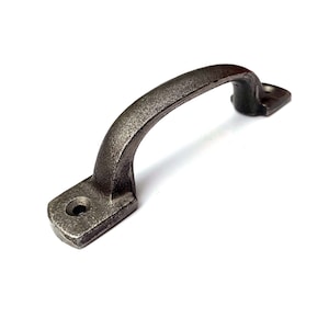 May include: A cast iron drawer pull with a dark grey finish. The pull has a rounded top and a rectangular base.