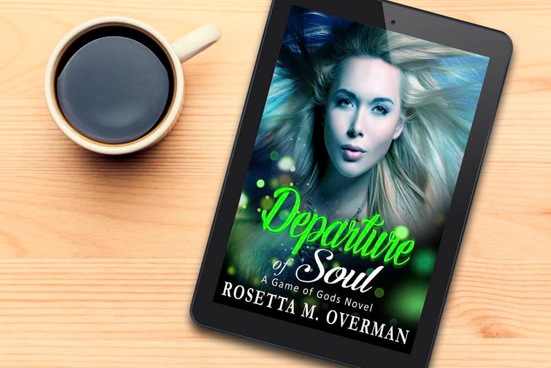 May include: A digital tablet displays the cover of the book "Departure of Soul: A Game of Gods Novel" by Rosetta M. Overman. The cover features a woman with blonde hair and the title in green script. A cup of coffee sits to the left.