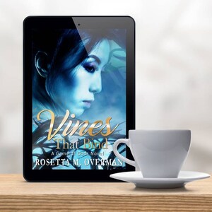 May include: A digital tablet displays the book cover of "Vines That Bind" by Rosetta M. Overman. The cover features a woman's profile in blue tones. A white teacup and saucer sit on a wooden surface.