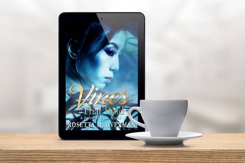 May include: A digital tablet displays the book cover of "Vines That Bind" by Rosetta M. Overman. The cover features a woman's profile in blue tones. A white teacup and saucer sit on a wooden surface.