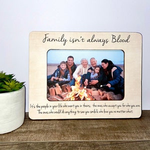 May include: A wooden photo frame with the text "Family isn't always Blood" and a photo of a family gathered around a campfire. The text below the photo reads "It's the people in your life who want you in theirs; the ones who accept you for who you are. The ones who would do anything to see you smile & who love you no matter what."