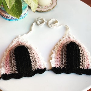 Puede incluir: Un top de bikini de crochet con un diseño degradado en rosa, marrón y negro. El top tiene un ribete de crochet blanco y tirantes ajustables.
