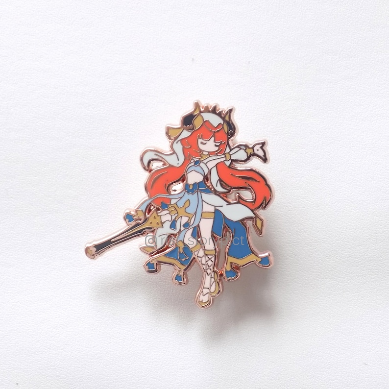 Puede incluir: Pin de esmalte de oro rosa con un personaje de dibujos animados con cabello rojo largo, vestido con un vestido blanco y azul y sosteniendo una espada. El personaje tiene una corona y cuernos en la cabeza.