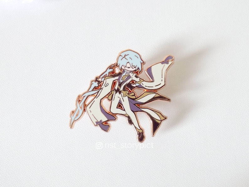 May include: A gold-toned enamel pin featuring a cartoon character with white hair, wearing a white and purple outfit, and holding a white and gold staff. The character is in a dynamic pose with their arms outstretched. The pin has a white background and the text "@nst_storypict" is visible in the bottom right corner.