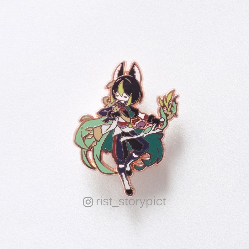 Puede incluir: Un pin de esmalte verde, negro y dorado con un personaje de dibujos animados con cabello negro y un atuendo verde y dorado. El personaje sostiene un bast&oacute;n verde y dorado. El pin est&aacute; sobre un fondo blanco. &copy;rist_storypict