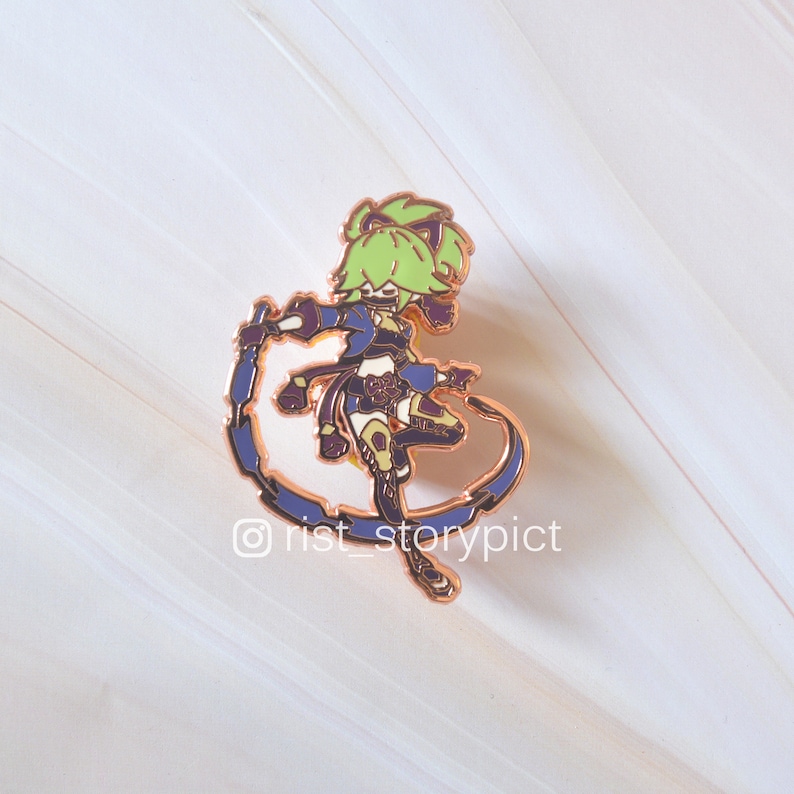 May include: A gold-colored enamel pin featuring a green-haired character with a blue and purple outfit, holding a weapon and standing in a dynamic pose. The pin is on a white background.