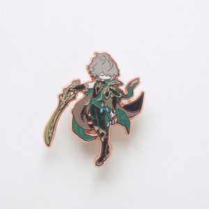 Puede incluir: Un pin de esmalte de color dorado que representa a un personaje con ropa verde y marr&oacute;n, cabello gris y una espada. El personaje est&aacute; en una pose din&aacute;mica con la espada levantada.