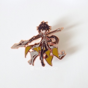 May include: A rose gold enamel pin featuring a cartoon character holding a spear. The character has black hair, a black coat, and yellow accents. The pin is on a white background.