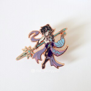 May include: A rose gold enamel pin featuring a character with purple and blue clothing holding a spear with a green and gold star at the end. The character has black hair and blue eyes. The pin has the text "@rist_storypict" at the bottom.