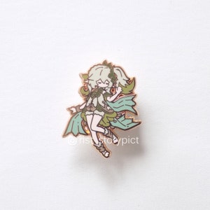Puede incluir: Un pin de esmalte dorado con un personaje de dibujos animados con cabello verde, un atuendo verde y marr&oacute;n y una capa verde. El personaje sonr&iacute;e y tiene una expresi&oacute;n juguetona.