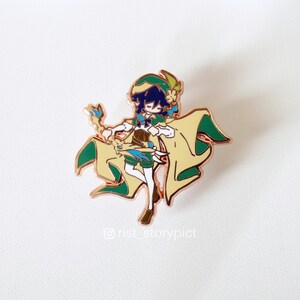 May include: A gold-colored enamel pin featuring a cartoon character with green and yellow clothing, a blue hat, and a green staff. The character has dark blue hair and is holding a staff with a blue and yellow gem. The pin is on a white background.