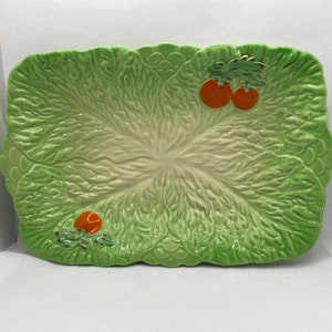May include: A green ceramic serving dish shaped like a lettuce leaf with three orange painted tomatoes.