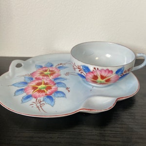 May include: A vintage teacup and saucer set. The light blue set features pink and red floral designs with blue leaves. The saucer has a unique shape with a handle. The cup has a matching floral design.