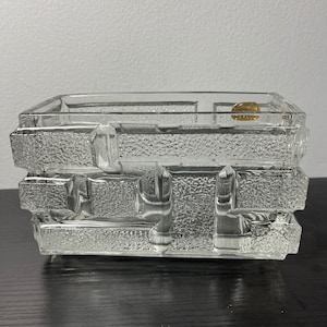 May include: A clear glass rectangular dish with a textured surface. The dish is made of stacked blocks of glass.