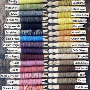 May include: A collection of colorful embroidery floss wound on wooden spools. The floss colors range from vibrant yellows and greens to deep blues, purples, and warm oranges, with labels indicating each color's name.