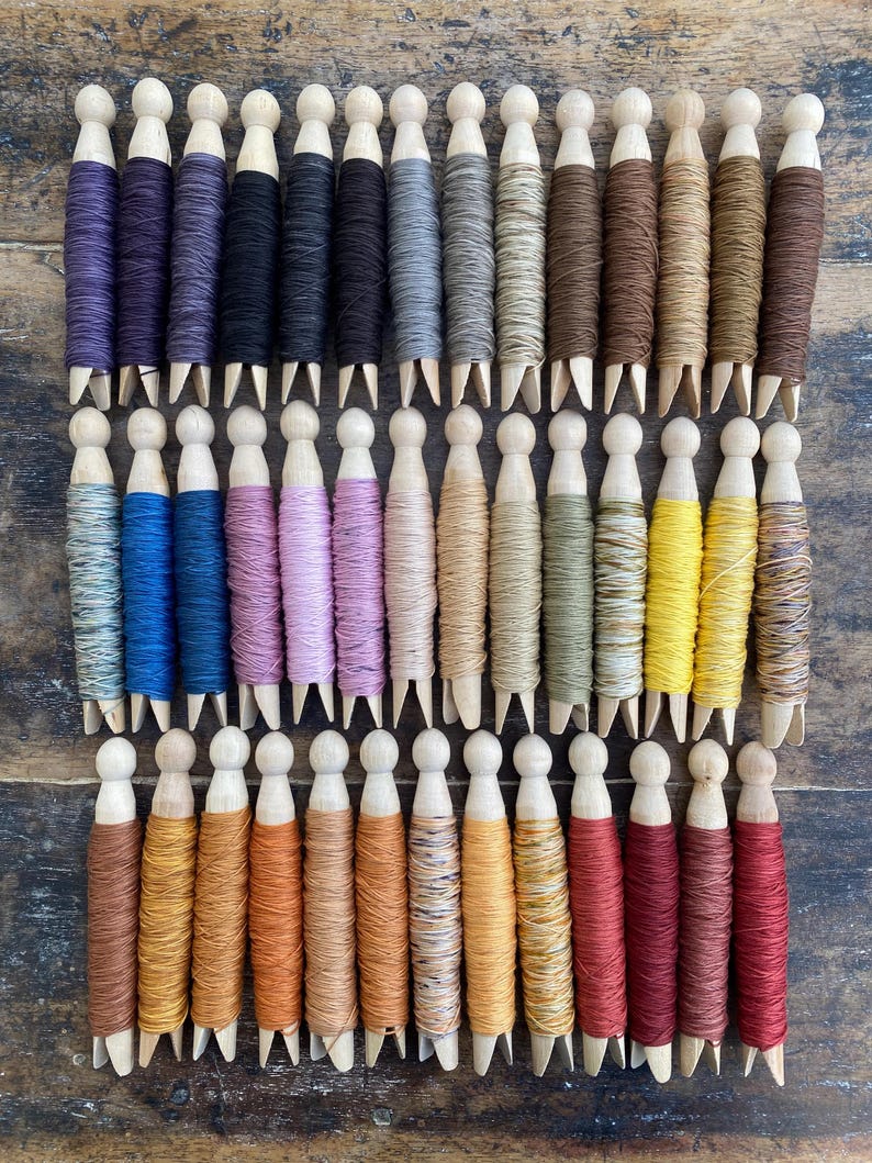 Pu&ograve; includere: Una collezione di mollette da bucato in legno avvolte con filo da ricamo di vari colori, disposte in tre file orizzontali. I fili presentano un ampio spettro di tonalit&agrave; tra cui viola, blu, rosa, giallo, marrone e rosso.