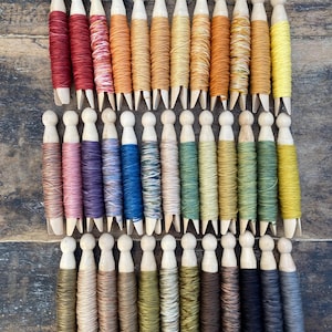 May include: A collection of thirty-three wooden clothespins, each wrapped with a different color of embroidery thread. The threads display a wide spectrum of colors including reds, oranges, yellows, blues, greens, browns, grays, and blacks.