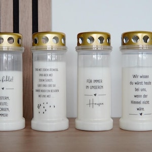 Könnte beinhalten: Vier weiße Glas-Kerzenhalter mit goldenen Deckeln und verschiedenen Textnachrichten. Die Textnachrichten lauten "Du fehlst! Gestern, Heute; Morgen, Immer!"  "Und mit jedem Atemzug und auch mit jedem Schritt, geht und lebst du immer noch ein bisschen mit uns mit..." "Für immer in unseren Herzen" and "Wir wissen du wärst heute bei uns, wenn der Himmel nicht wäre."