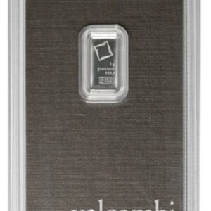May include: A platinum bar encased in a clear plastic holder. The bar is rectangular with a small logo and text. The holder sits on a dark gray background with the words "valcambi suisse" printed in white.