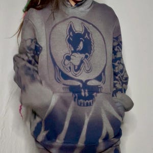 May include: Gray hoodie and sweatpants set with a blue wolf graphic on the front. The hoodie and sweatpants have a tie-dye effect with blue accents. The sweatpants feature a blue bear graphic.