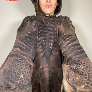 May include: A brown hooded sweatshirt with a black and white print of a tree and a geometric pattern. The sweatshirt has a large hood and a relaxed fit. The text "XL" is written in red on the top left corner of the image.