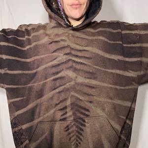 May include: A brown and black tie-dye hoodie with a fern pattern. The hoodie has a large pocket on the front and a drawstring hood.