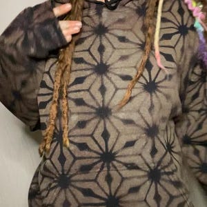 May include: A brown hoodie with a black geometric pattern. The hoodie has a drawstring hood and a kangaroo pocket.