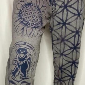 Puede incluir: Pantalones de chándal grises con un patrón geométrico azul y blanco, un girasol con un diseño de flor de la vida y un oso azul Grateful Dead.