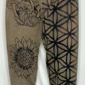 Könnte beinhalten: Braune Jogginghose mit schwarzen geometrischen und floralen Mustern. Die Muster umfassen einen Schmetterling, eine Sonnenblume, einen Farn und ein geometrisches Muster.