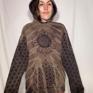 May include: A brown tie-dye hoodie with a black sunflower graphic featuring a geometric pattern. The hoodie has a large pocket on the front and black geometric patterns on the sleeves.