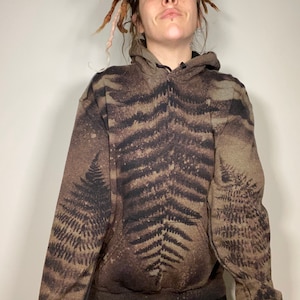 May include: A brown hooded sweatshirt with a fern leaf pattern. The sweatshirt has a drawstring hood and a kangaroo pocket.