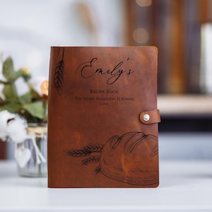 May include: A brown leather recipe book with the text "Emily's Recipe Book The Secret Ingredient Is Always Love" and a drawing of a loaf of bread and wheat stalks.
