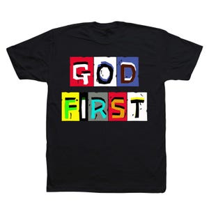 May include: Black t-shirt with the words "GOD FIRST" in a colorful, block letter design. The text is arranged in two rows, with each letter in a different color block. The shirt is made of a soft material.