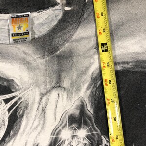 May include: A black and white graphic t-shirt featuring a hooded figure with glowing eyes and a chain. The shirt has a tag that reads "MEGA T" and "100% Cotton Made in China". The shirt measures approximately 28 inches in length.