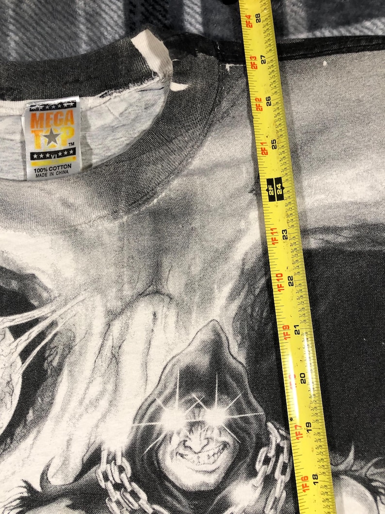 May include: A black and white graphic t-shirt featuring a hooded figure with glowing eyes and a chain. The shirt has a tag that reads "MEGA T" and "100% Cotton Made in China". The shirt measures approximately 28 inches in length.