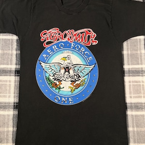May include: Black Aerosmith band t-shirt featuring a circular design with a white eagle, blue wings, and the text "Aero Force One." The band's name is in red and white above the design.