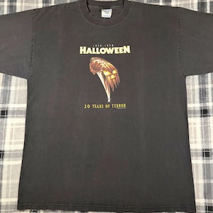 May include: Dark gray t-shirt featuring the text "HALLOWEEN" above a graphic of a knife and pumpkin. The text "20 YEARS OF TERROR" is below the graphic. The shirt is a vintage style and is likely a collectible item.