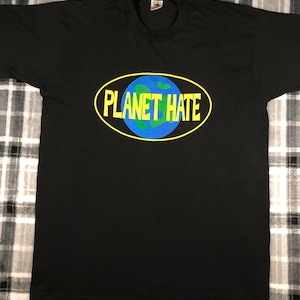 May include: Black t-shirt with a graphic that says "PLANET HATE" in yellow text inside a yellow oval. The graphic includes a blue circle with green continents, resembling Earth.