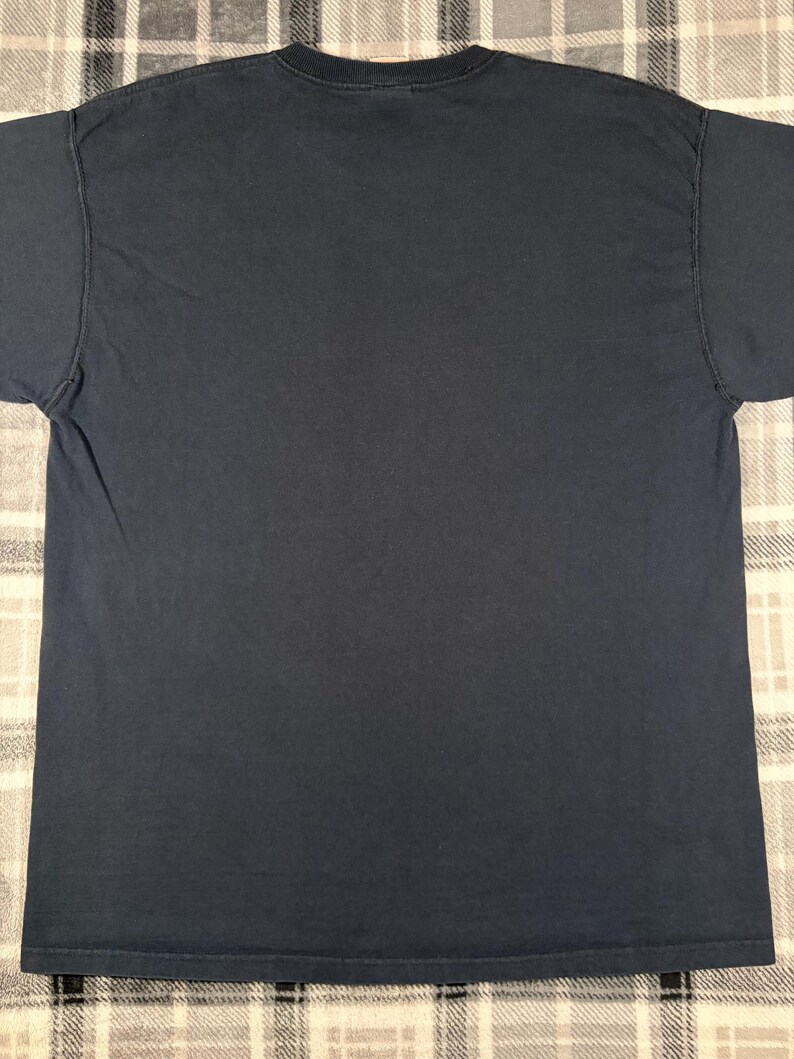 May include: A solid dark navy blue short-sleeved t-shirt featuring a classic crew neckline. The garment is constructed with a standard fit, short sleeves, and a straight hemline, presenting a plain and unadorned surface on the back side.