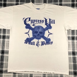 May include: White t-shirt with a blue graphic of a skull and crossbones with the text "Cypress Hill Skull & Bones".