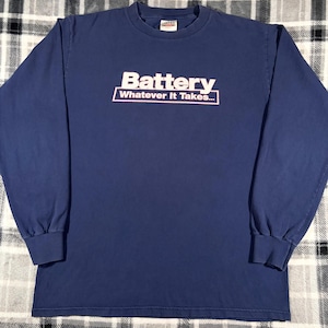 May include: A long-sleeved, navy blue shirt with the word "Battery" in white block letters above the phrase "Whatever It Takes..." in a white, underlined font. The shirt has a crew neck and long sleeves.