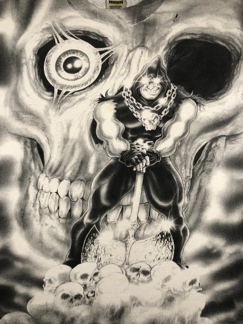 May include: A black and white graphic tee featuring a muscular figure in a hooded cloak, holding an axe, and standing on a pile of skulls. A large skull and an eye are in the background. The design is detailed and has a dark, gothic theme.