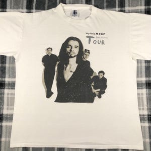 May include: White t-shirt featuring a black and white graphic of the band Depeche Mode. The graphic includes the band members and the text "Depeche Mode Devotional Tour". The shirt is made of a soft, likely cotton material.