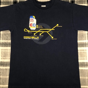 May include: Navy blue t-shirt featuring a yellow and white graphic of a map with the text "COACHELLA" and "STATIONS OPEN 11 AM - 12 MIDNIGHT". The graphic includes a ticket design with the number "05".
