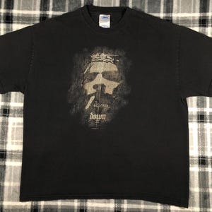 May include: Black t-shirt with a distressed graphic of a face with a crown of thorns and the word "down" in a stylized font. The shirt is made of a soft material and has a crew neck.