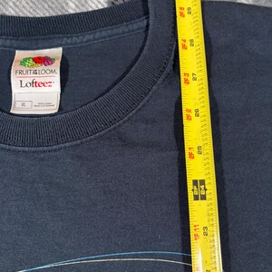 May include: A dark navy blue t-shirt with a crew neckline and a Fruit of the Loom Lofteez label indicating size XL. A yellow measuring tape is placed vertically along the fabric, showing a length measurement extending past 30 inches.