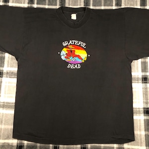 May include: Black long-sleeve t-shirt with an embroidered Grateful Dead logo featuring a dancing skeleton in a red and yellow costume. The logo is surrounded by a circle with the words "Grateful Dead" in white.