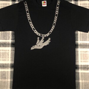 May include: Black t-shirt featuring a silver chain necklace design with a pendant of a bird in flight. The shirt is made of a soft material and has a crew neck. The Fruit of the Loom logo is visible on the upper back.